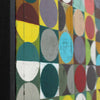 Close-up side view of a colourful geometric wall art piece with overlapping circles and half-circles in yellow, teal, red, grey, purple, green, and white on a dark background.