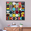 A square black framed abstract artwork featuring a grid of colourful circles and half-circles in many bright tones on a grid background the painting is hanging on a light grey wall.