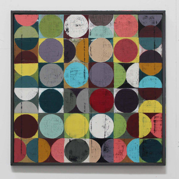 A square framed abstract artwork featuring a grid of colorful circles and half-circles in many muted and bright tones on a white wall.