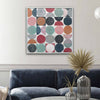 A square framed wall art print featuring a grid of colorful circles in muted pink, teal, navy, orange, gray, and red tones, displayed above a dark blue sofa in a styled living room.