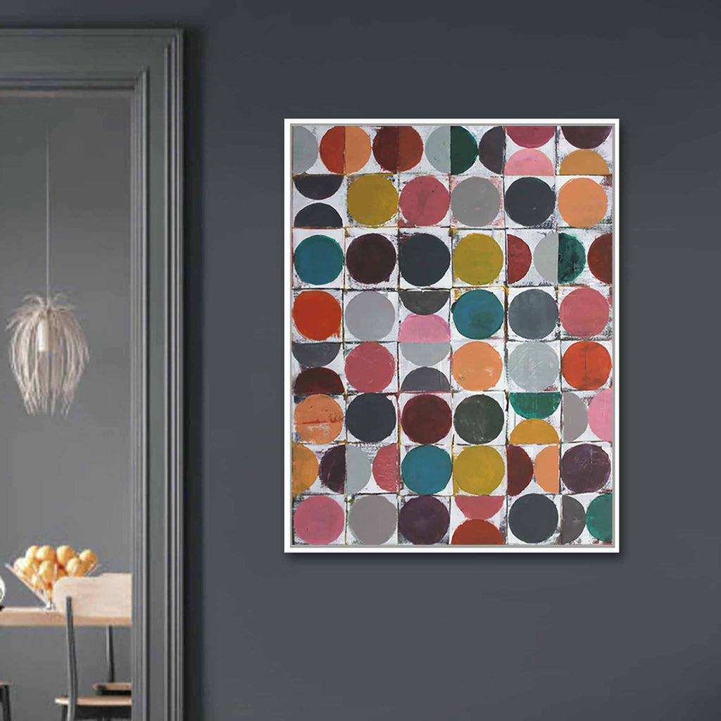 A framed abstract art print featuring a grid of colorful circles in various shades, hung on a dark gray wall in a modern interior setting.