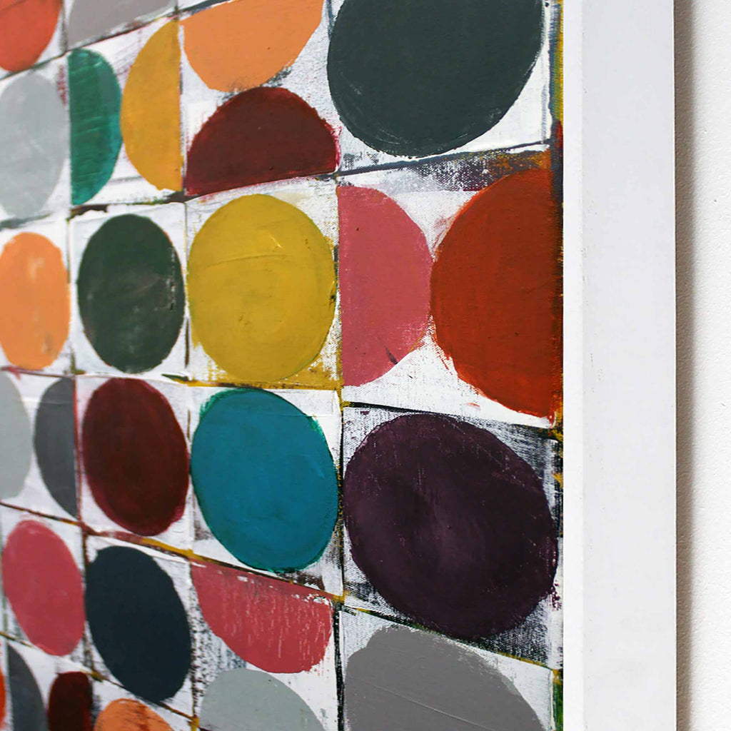Close-up of a colorful abstract wall art piece showing painted circles and arcs in orange, yellow, red, teal, purple, green, and gray on a white grid, with a white frame edge visible on the right.
