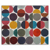A square abstract art painting featuring a grid of colourful circles and semicircles in red, pink, yellow, blue, teal, grey, and navy on a white background, shown against a plain white studio wall.