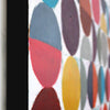 Close-up side view of a colourful abstract artwork featuring overlapping painted circles and semicircles in muted blue, red, purple, yellow, grey, and brown tones on a white background.